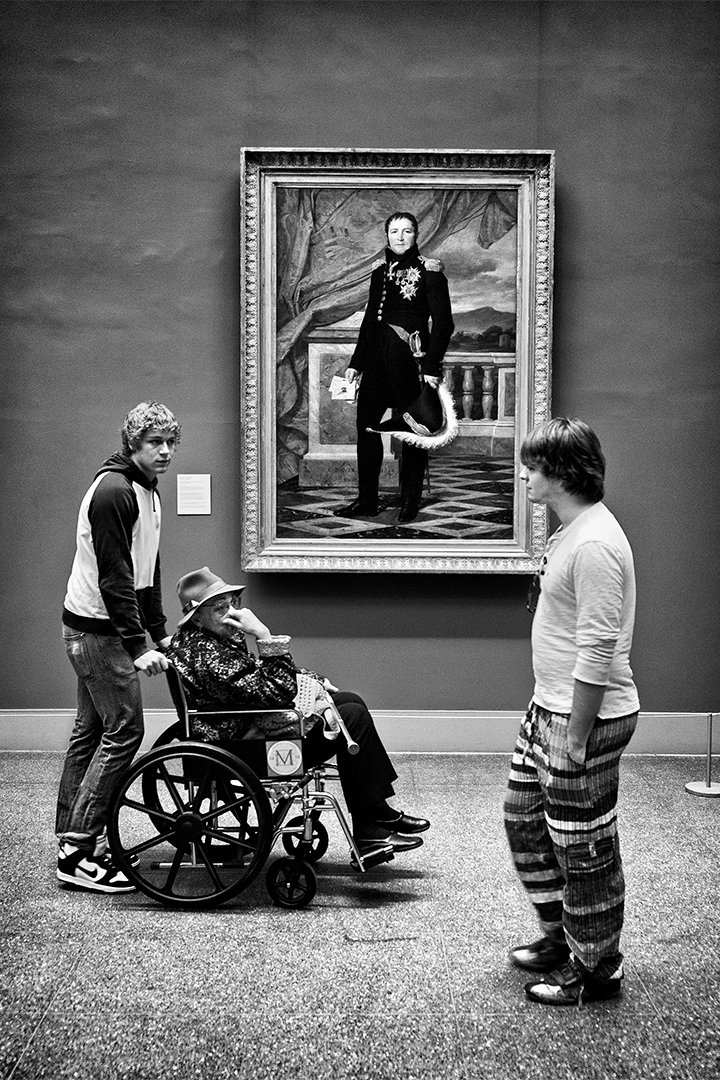 Visitors and a wheelchair in front of a painting in a museum.